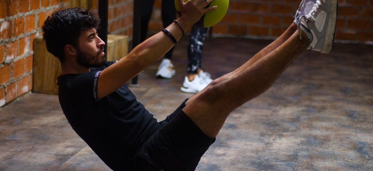 Focused man performing core exercises with a medicine ball in an indoor gym highlighting fitness and strength.